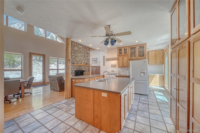 kitchen featuring a sink, open floor plan, white refrigerator with ice dispenser, a stone fireplace, and an island with sink