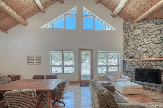 living area with beam ceiling, wood ceiling, hardwood / wood-style flooring, a stone fireplace, and high vaulted ceiling