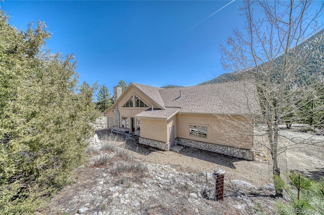 view of property exterior with stucco siding, stone siding, a chimney, and a shingled roof
