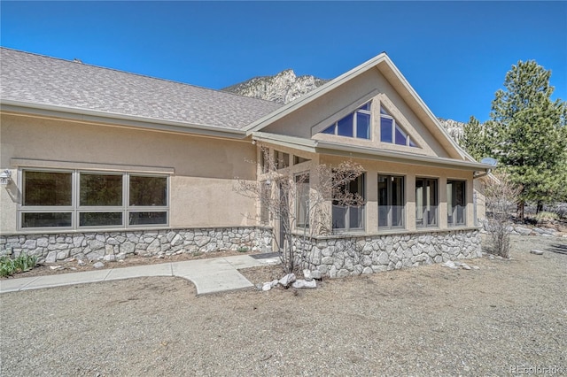 back of property with roof with shingles, a porch, stone siding, and stucco siding