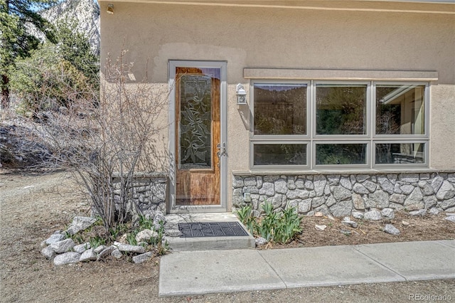 doorway to property with stone siding and stucco siding