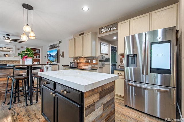 kitchen with decorative light fixtures, tasteful backsplash, a center island, light wood-type flooring, and stainless steel fridge