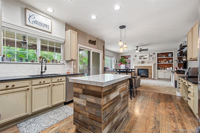 kitchen with pendant lighting, sink, hardwood / wood-style flooring, stainless steel dishwasher, and cream cabinetry