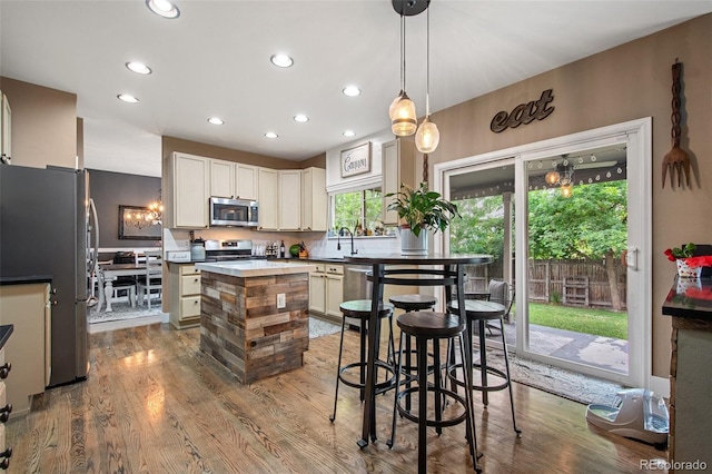 kitchen with pendant lighting, a center island, sink, hardwood / wood-style flooring, and appliances with stainless steel finishes