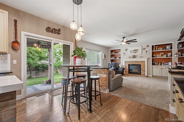 dining space with a brick fireplace, wood-type flooring, built in features, and ceiling fan