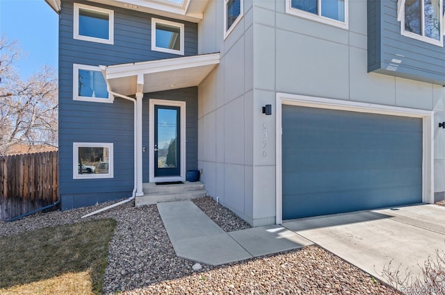 entrance to property featuring an attached garage, fence, and driveway