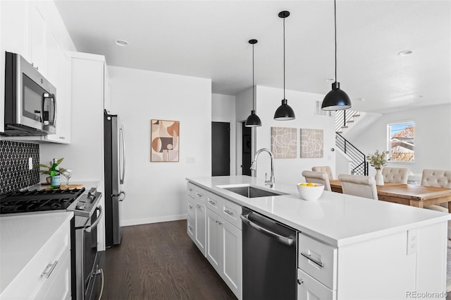 kitchen with dark wood-type flooring, a kitchen island with sink, a sink, white cabinetry, and stainless steel appliances