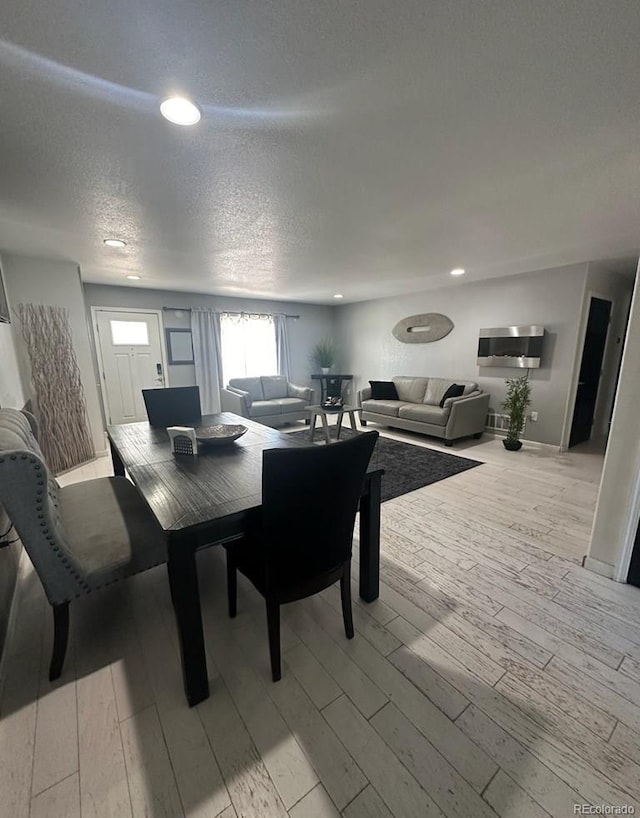 dining area featuring light wood-type flooring, recessed lighting, a textured ceiling, and baseboards