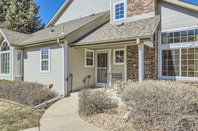 view of exterior entry with brick siding and a shingled roof