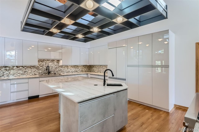 kitchen with a center island with sink, light hardwood / wood-style flooring, sink, and white cabinets