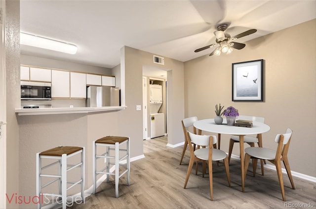 dining room featuring light hardwood / wood-style floors, stacked washer and clothes dryer, and ceiling fan