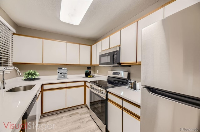 kitchen with sink, white cabinetry, light hardwood / wood-style flooring, a textured ceiling, and appliances with stainless steel finishes