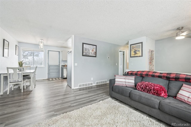 living room featuring ceiling fan, a textured ceiling, and dark wood-type flooring