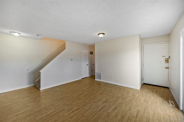 unfurnished living room with baseboards, visible vents, wood finished floors, and stairway
