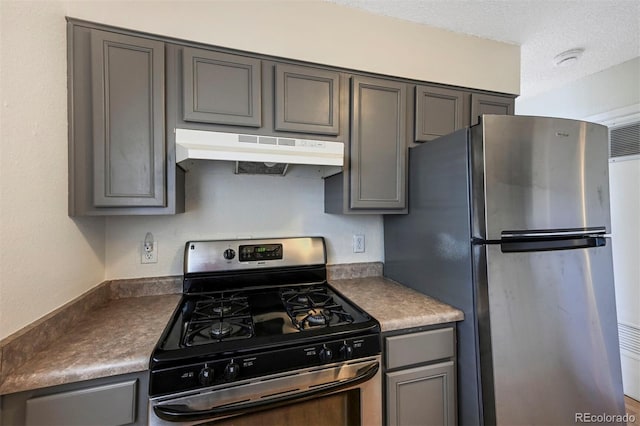 kitchen featuring gray cabinetry, dark countertops, under cabinet range hood, and appliances with stainless steel finishes