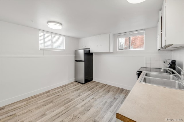 kitchen with sink, white cabinetry, light wood-type flooring, stainless steel appliances, and decorative backsplash