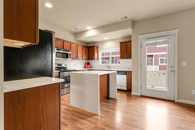 18061 E Saskatoon Pl, Parker, CO 80134 - kitchen featuring appliances with stainless steel finishes, light wood-style flooring, tasteful backsplash, a center island, and light countertops