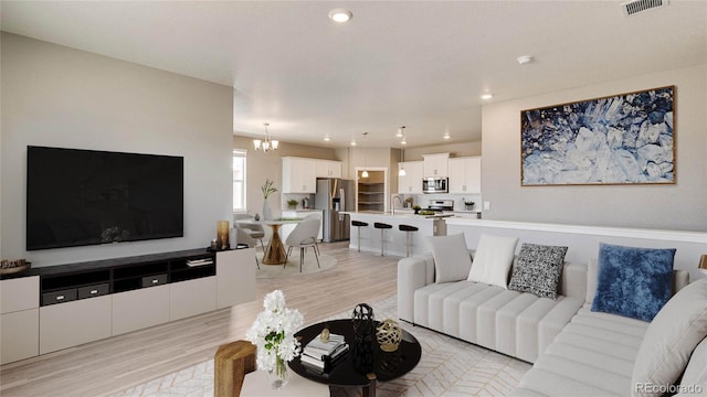 living room with sink, an inviting chandelier, and light hardwood / wood-style flooring