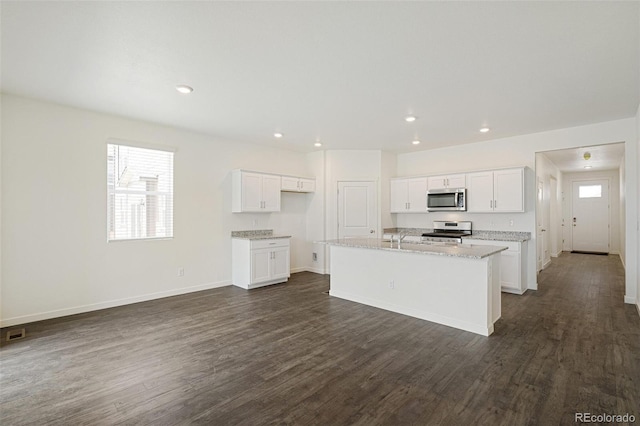 kitchen with appliances with stainless steel finishes, light stone counters, dark wood-type flooring, a center island with sink, and white cabinets