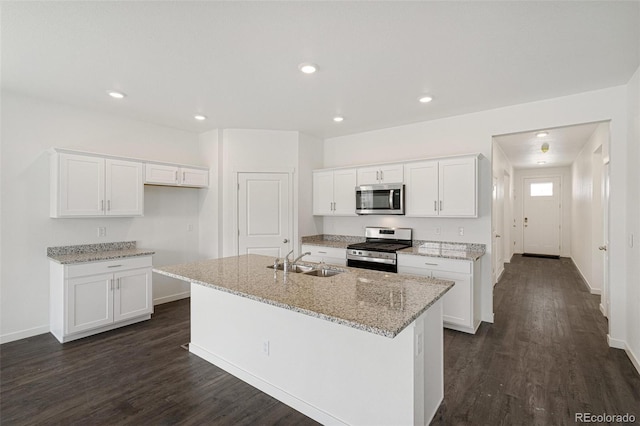 kitchen with light stone countertops, stainless steel appliances, a kitchen island with sink, sink, and white cabinets