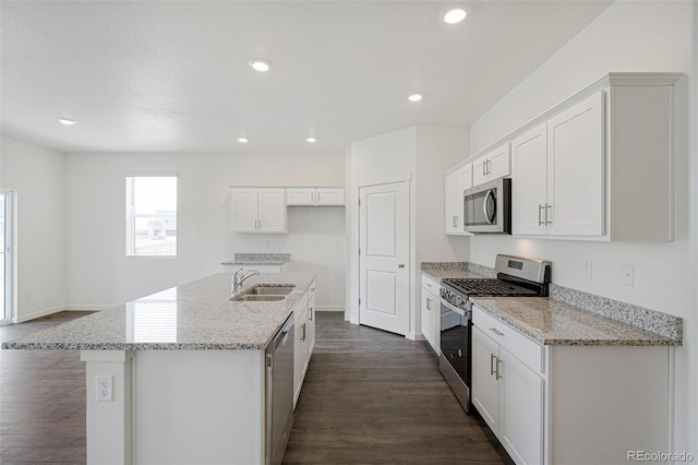 kitchen with light stone counters, stainless steel appliances, a kitchen island with sink, sink, and white cabinetry