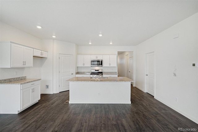 kitchen with light stone countertops, stainless steel appliances, dark wood-type flooring, white cabinets, and an island with sink