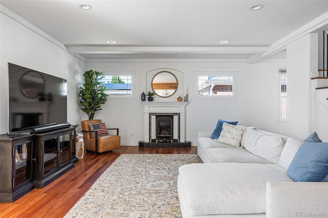 living room featuring beam ceiling, a tile fireplace, a healthy amount of sunlight, and hardwood / wood-style flooring