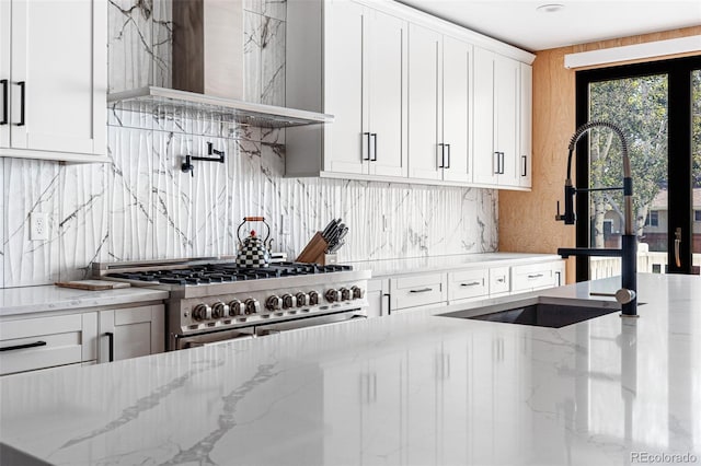 kitchen with light stone counters, wall chimney exhaust hood, stainless steel range, sink, and white cabinetry