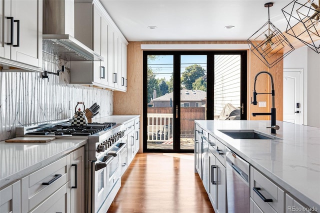 kitchen with pendant lighting, sink, wall chimney exhaust hood, white cabinetry, and stainless steel appliances