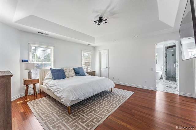 bedroom with a tray ceiling, ensuite bath, and dark hardwood / wood-style floors