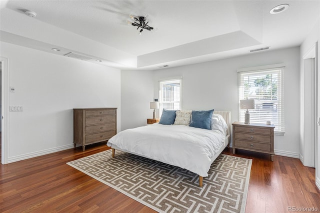 bedroom with a tray ceiling, multiple windows, and dark wood-type flooring