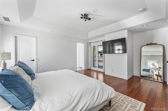 bedroom with access to exterior, dark hardwood / wood-style floors, and a tray ceiling