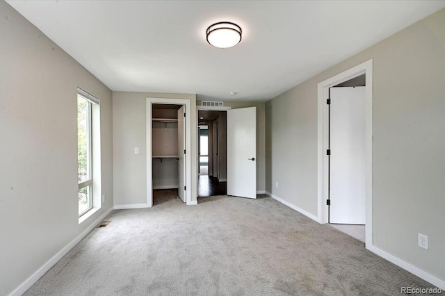 unfurnished bedroom with light colored carpet, a closet, and a walk in closet