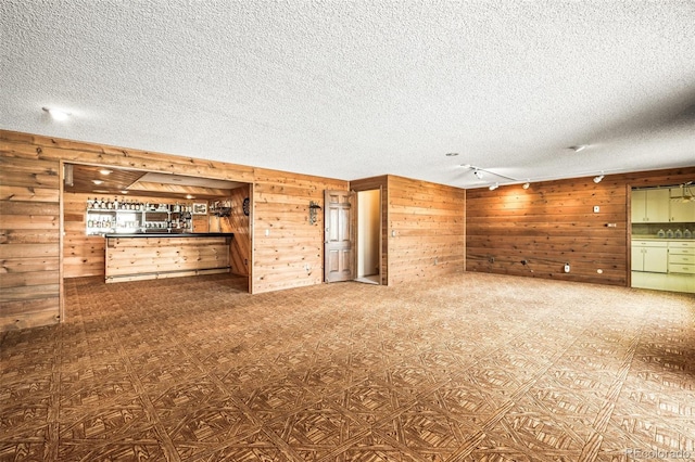 unfurnished living room featuring wooden walls, rail lighting, a textured ceiling, and bar area