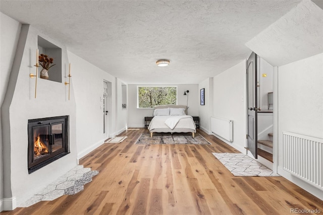 1669 Apple Valley Rd, Lyons, CO 80540 - bedroom with radiator, a glass covered fireplace, wood finished floors, a textured ceiling, and baseboards