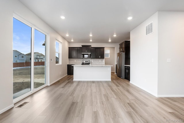 kitchen featuring decorative backsplash, light hardwood / wood-style floors, stainless steel appliances, and a kitchen island with sink