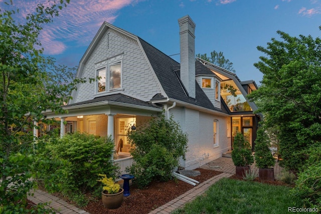 back of property with brick siding, a gambrel roof, a shingled roof, and covered porch