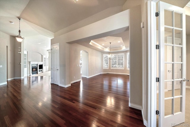 unfurnished living room with baseboards, arched walkways, dark wood finished floors, and a notable chandelier