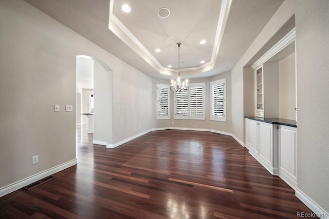 unfurnished dining area with arched walkways, a tray ceiling, dark wood finished floors, and visible vents