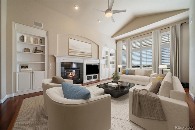 living area featuring ceiling fan, a glass covered fireplace, built in shelves, wood finished floors, and lofted ceiling