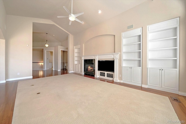 unfurnished living room featuring a ceiling fan, visible vents, wood finished floors, built in shelves, and a glass covered fireplace