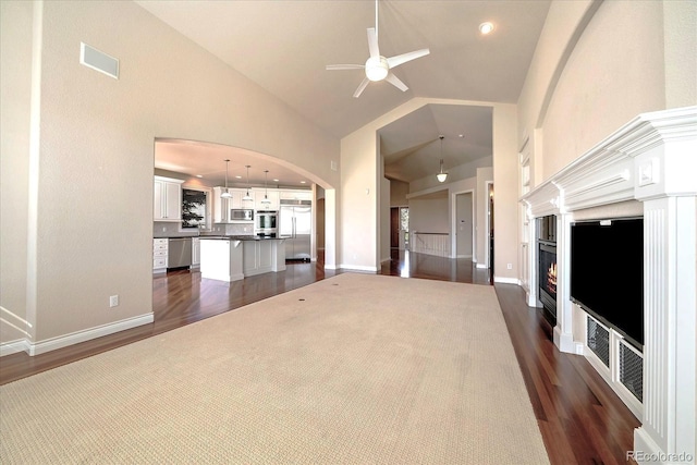 unfurnished living room featuring a ceiling fan, arched walkways, dark wood-style floors, and high vaulted ceiling