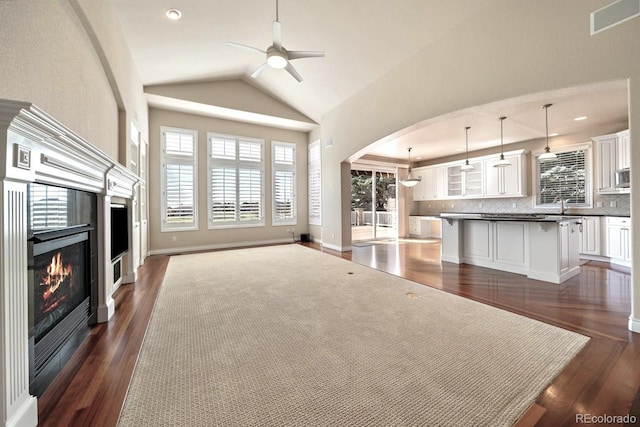 unfurnished living room with arched walkways, ceiling fan, a glass covered fireplace, and dark wood-style floors