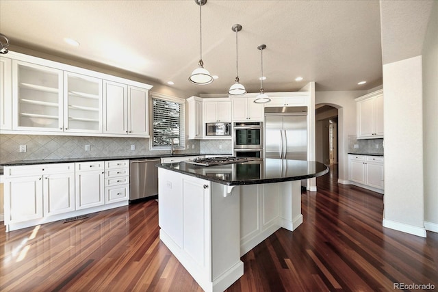 kitchen with backsplash, a center island, arched walkways, dark wood finished floors, and built in appliances