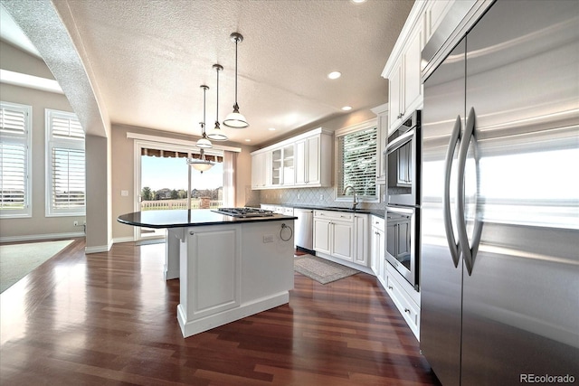 kitchen featuring dark countertops, appliances with stainless steel finishes, a sink, a textured ceiling, and a center island