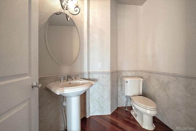 half bathroom featuring wood finished floors, toilet, tile walls, a wainscoted wall, and a sink