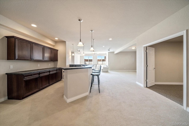 kitchen with dark brown cabinetry, a breakfast bar, open floor plan, light colored carpet, and hanging light fixtures