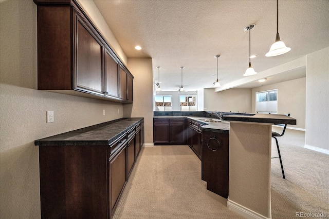 kitchen featuring a breakfast bar area, dark brown cabinets, light colored carpet, and a sink