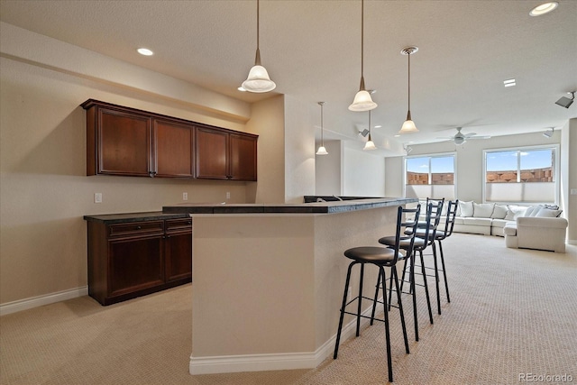 kitchen featuring baseboards, a kitchen breakfast bar, dark brown cabinets, and light colored carpet
