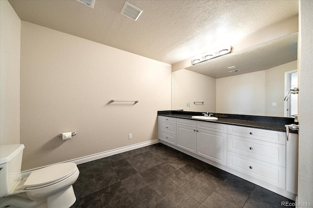 bathroom with a textured ceiling, visible vents, vanity, baseboards, and toilet